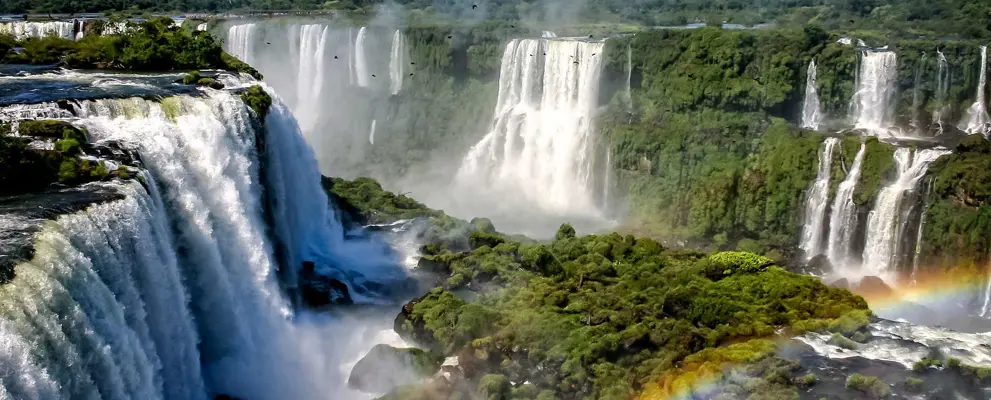 Water cascading over the Iguacu falls with rainbow in foreground in Brazil